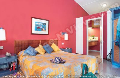 2 star hotel le coin de mire hotel standard room
2* Le Coin de Mire bedroom view. The standard bedroom is decorated in pinks and oranges. The bedroom leads onto a bathroom. The rooms are tastefully furnished in the local style of the island with cane and wooden furniture to convey a warm and welcoming atmosphere. 
Keywords: 2*hotel, standard bedroom, bed, pink, orange, bathroom, furnished, cane, woode, furniture
